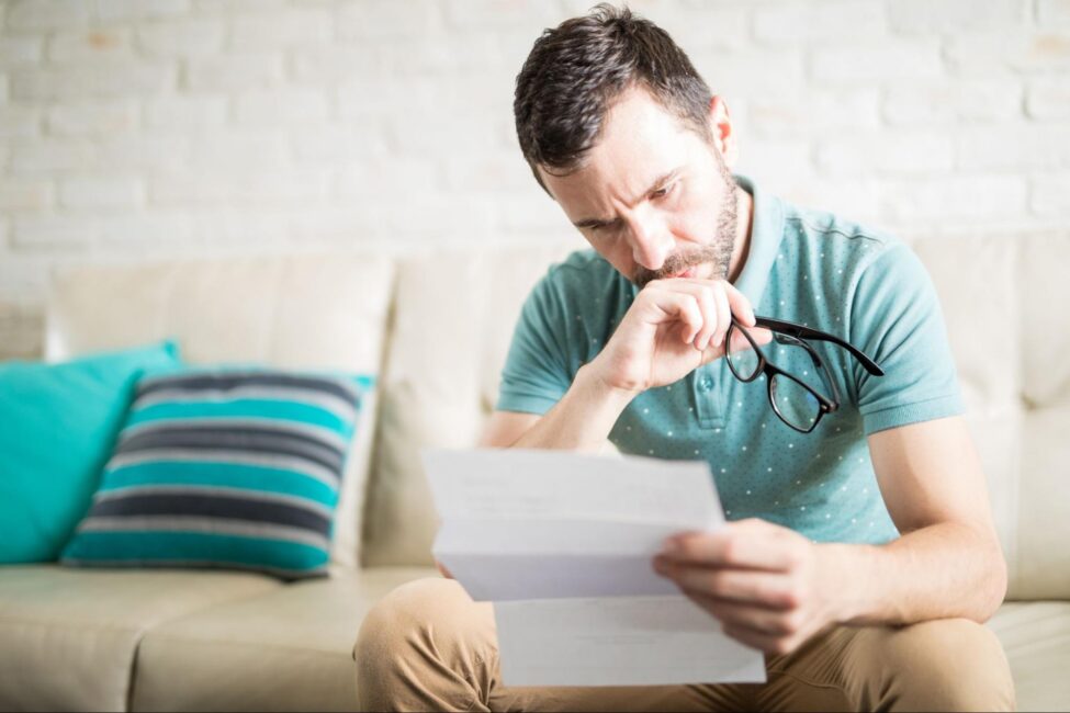 A man looks concerned while examining a bank statement at home