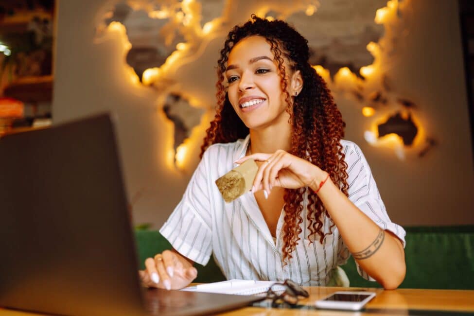 Young woman using a laptop while holding a balance transfer credit card to manage her finances