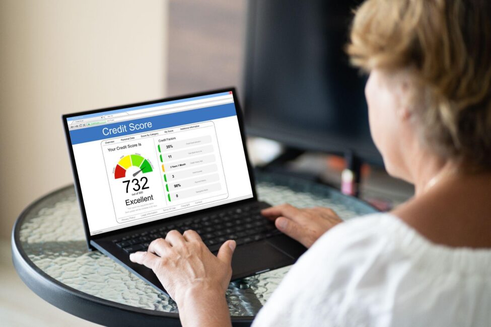 A woman sitting at a table using a laptop to check her credit score and monitor her financial health
