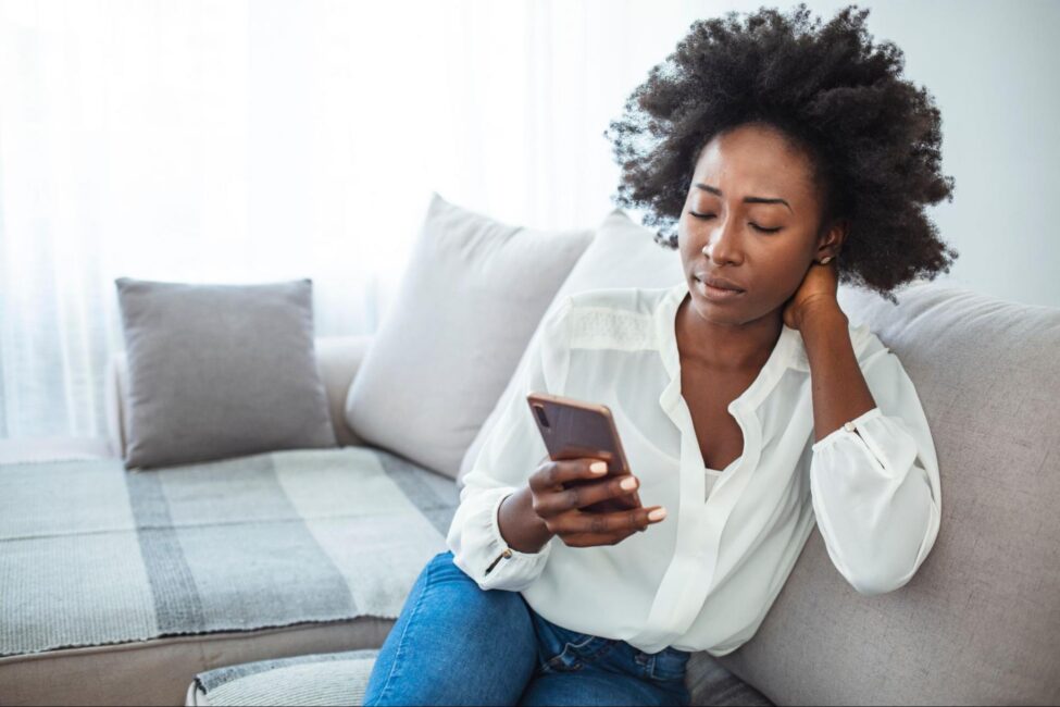 A woman sitting on the couch, looking focused as she uses her smartphone to determine why her mobile check deposit was rejected