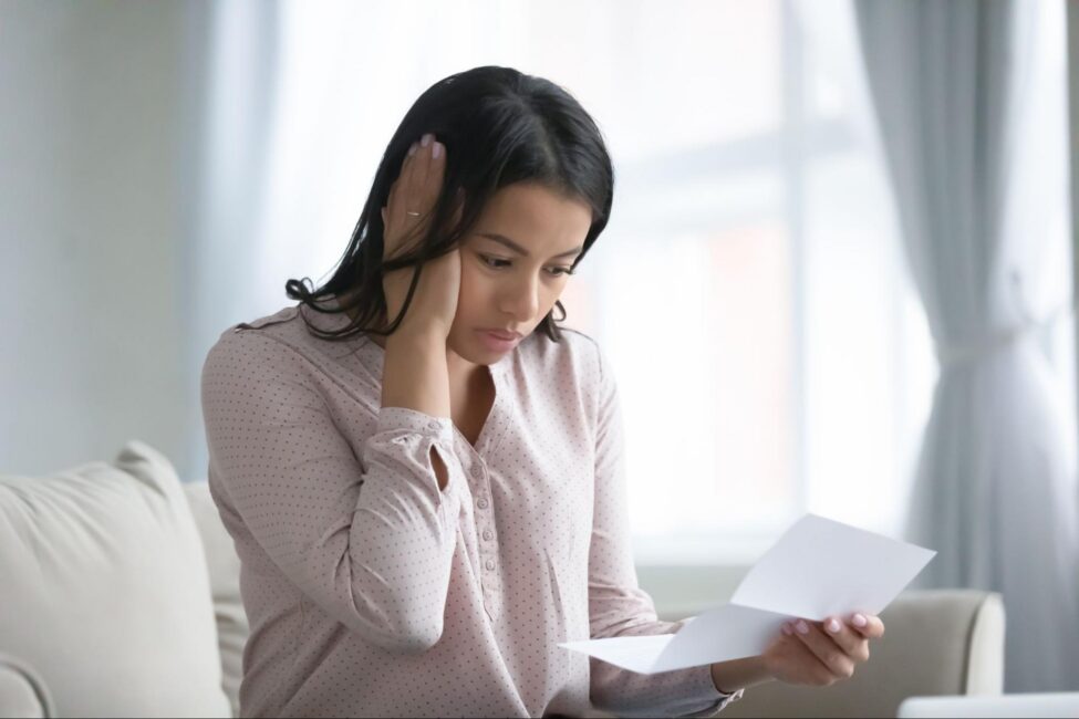 Worried woman holding her head while reading medical bills on a couch