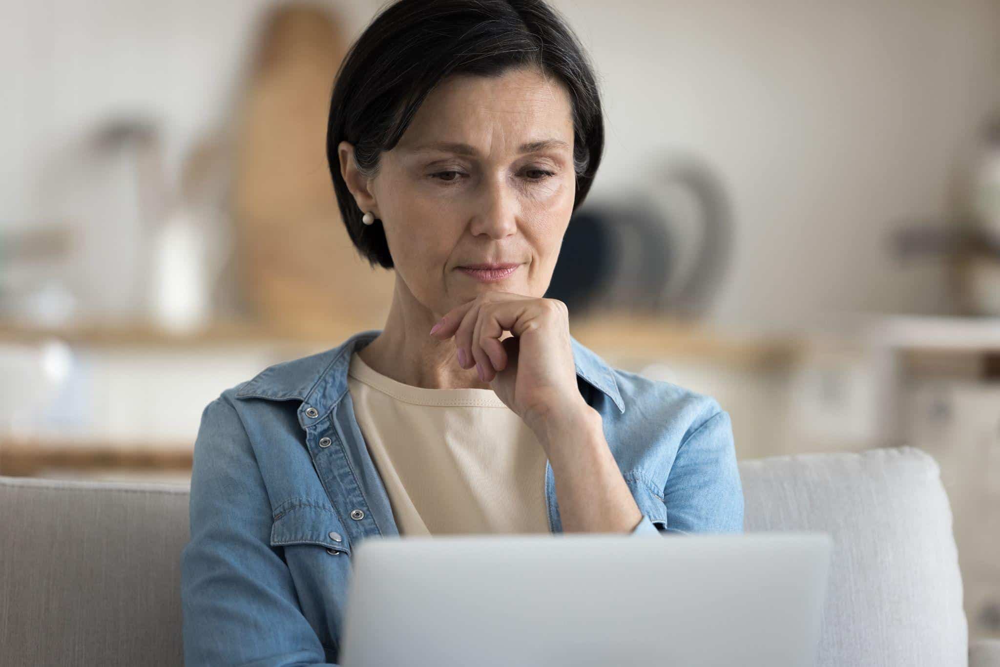 A focused woman thoughtfully researching personal line of credit loans on her laptop