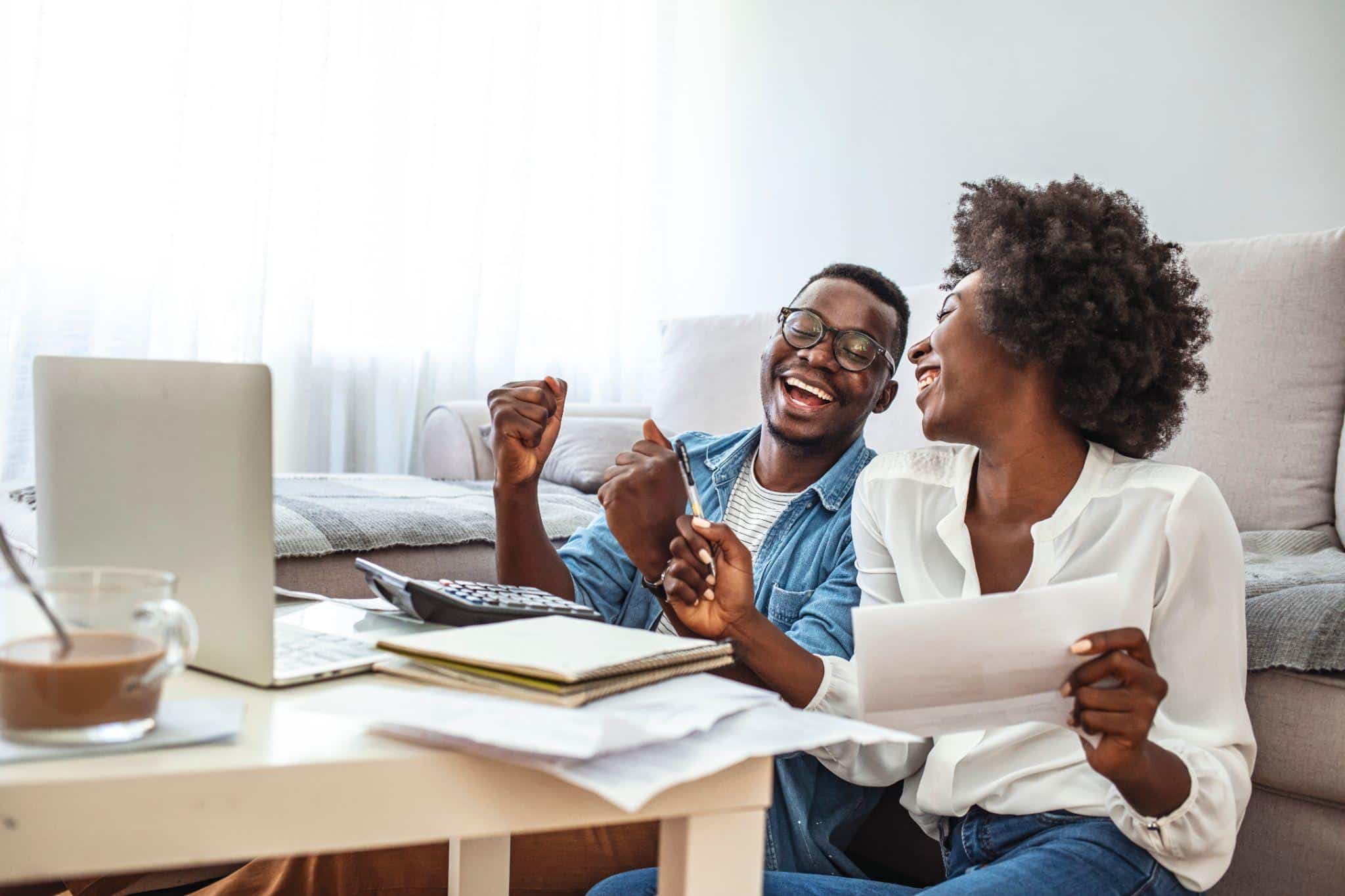 A laughing couple cheers while reviewing tax documents, relieved they no longer owe taxes