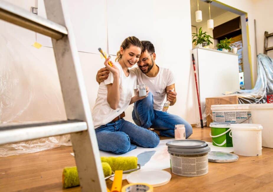 Happy couple sitting on the floor surrounded by paint cans and rollers as they begin a home improvement project