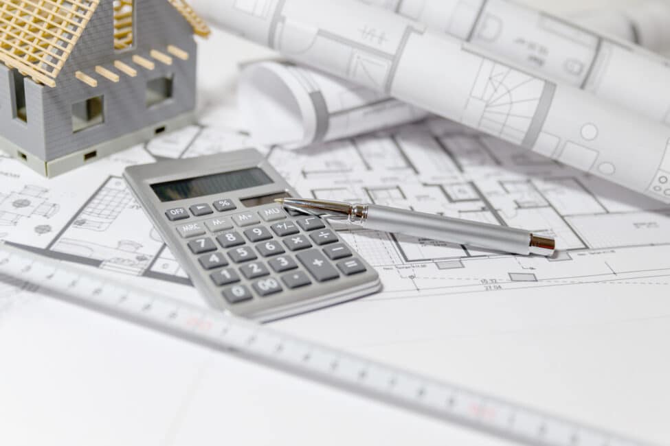 Calculator, pen, ruler, and miniature model house on architectural blueprints