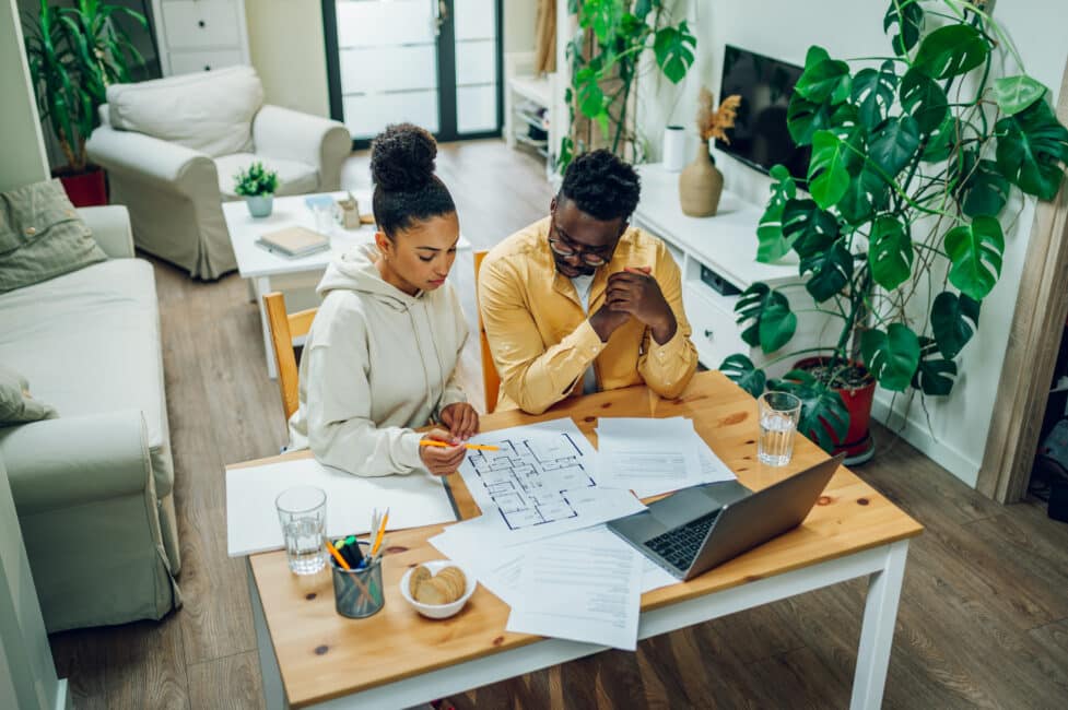 Couple reviewing home blueprints and documents at a table while planning a home renovation project